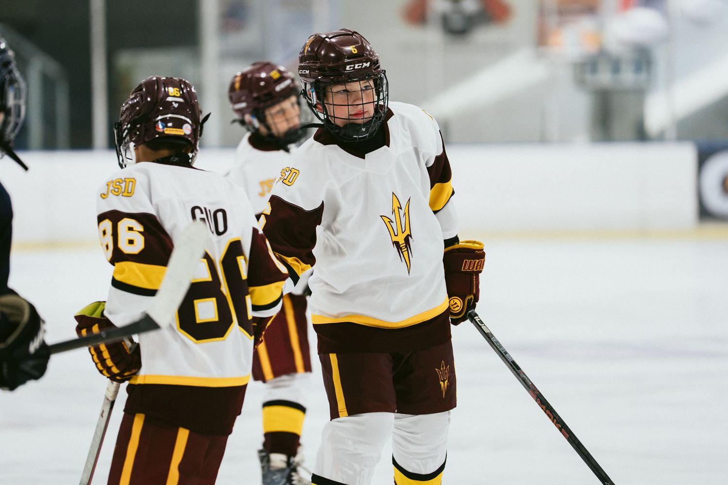 Two Arizona State Sun Devils hockey players in maroon and gold uniforms celebrate together on the ice rink.