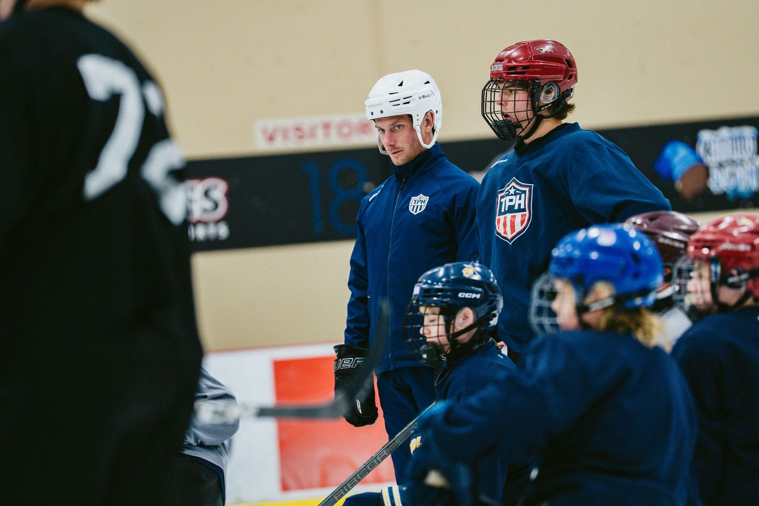 USA Hockey coaches and players in navy uniforms practice on ice rink during team training session.