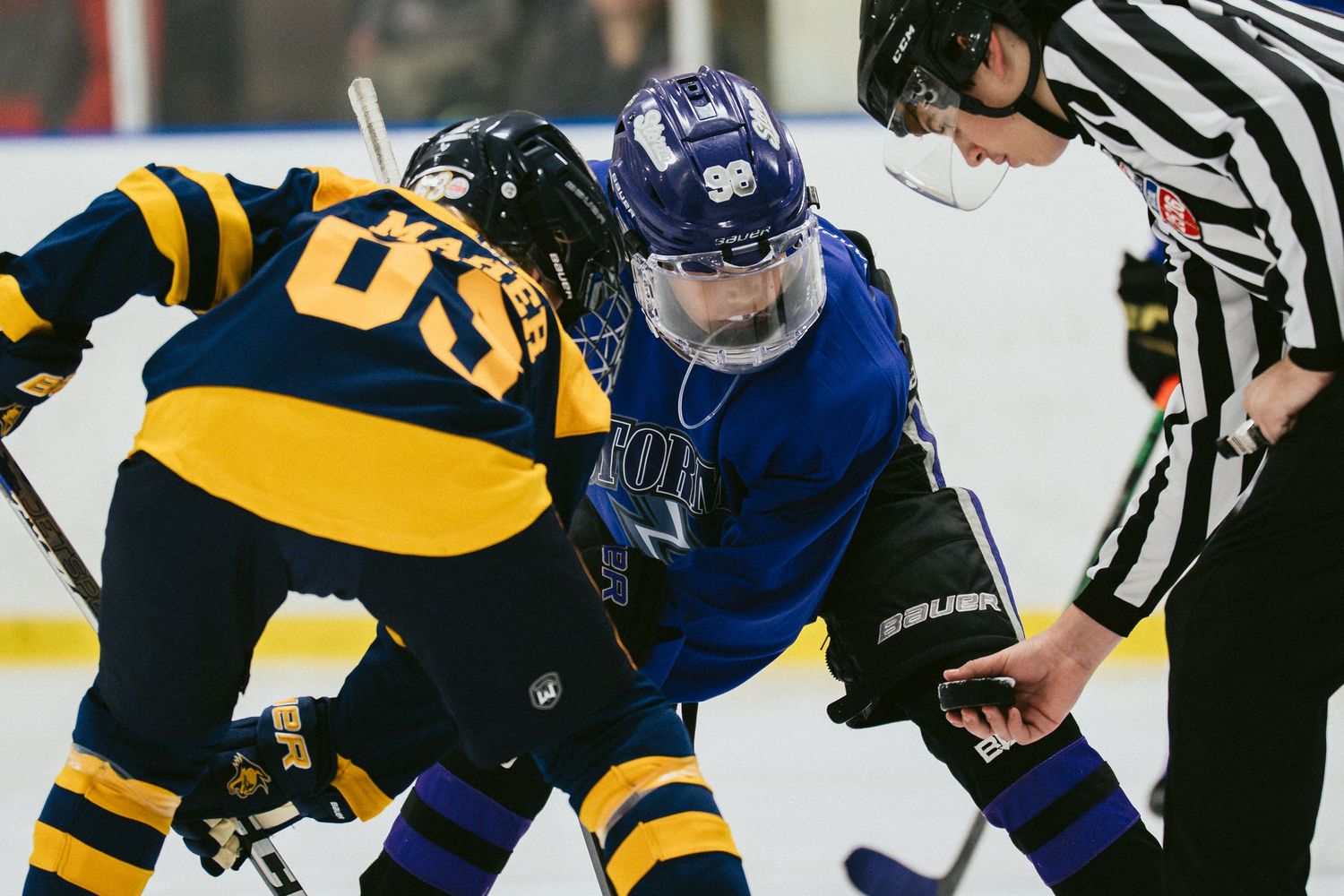 Two ice hockey players face off at a faceoff circle while a referee oversees the play during a competitive game.