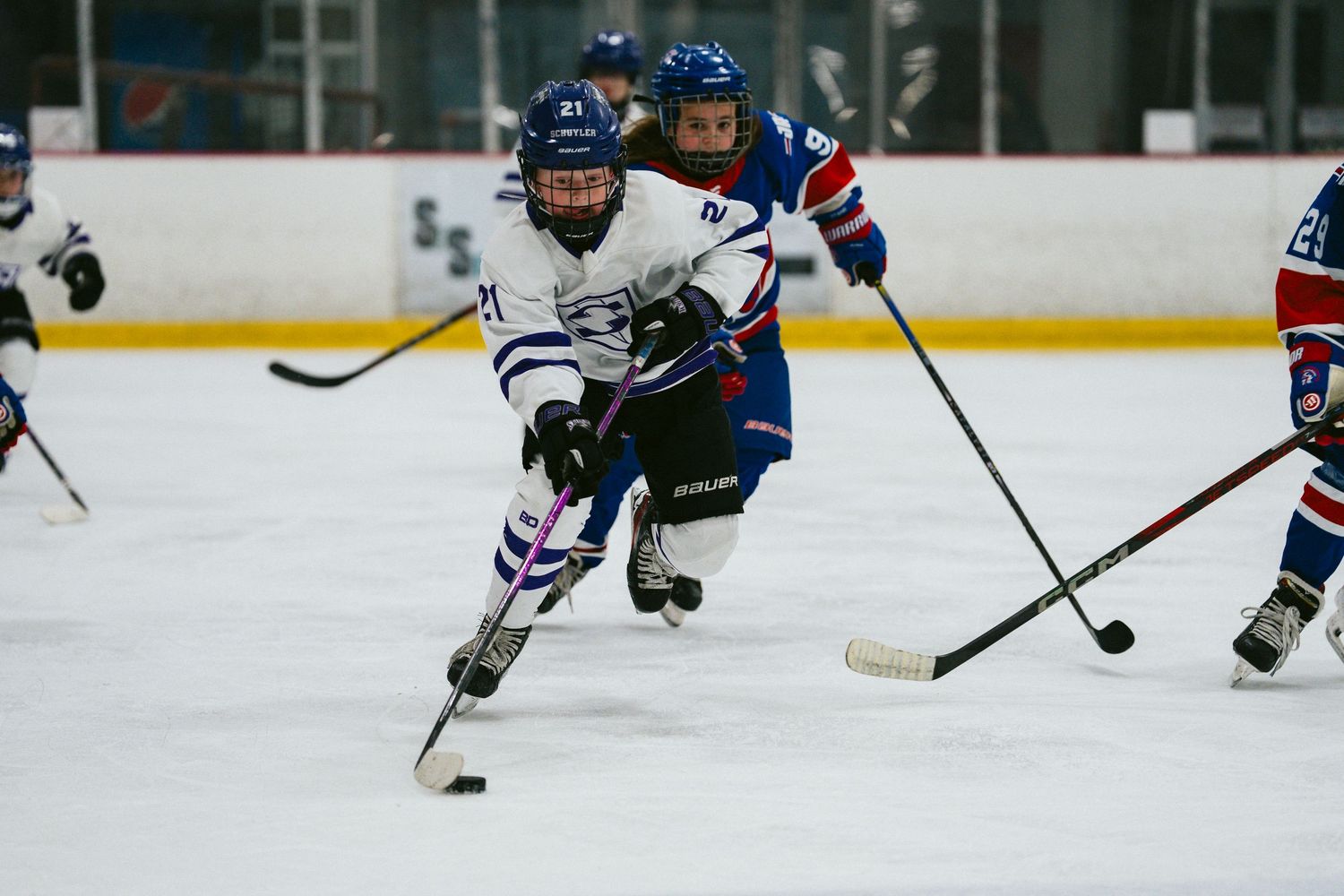 Hockey player in white jersey controls puck while being defended during intense game action.