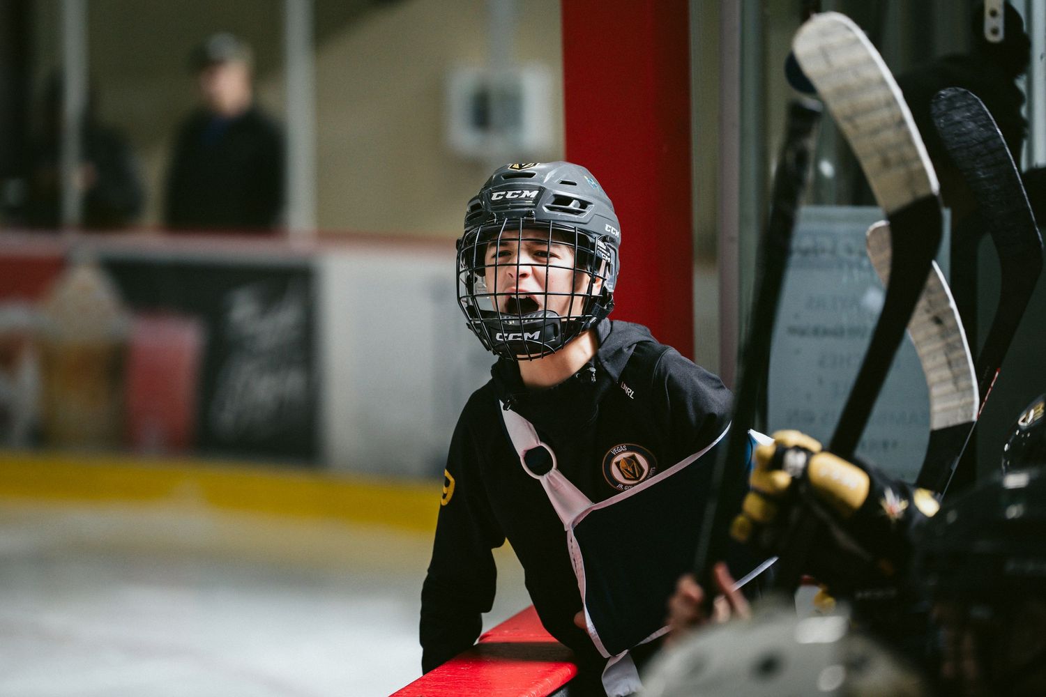 Hockey player in black uniform and protective gear watching from the bench during a game.