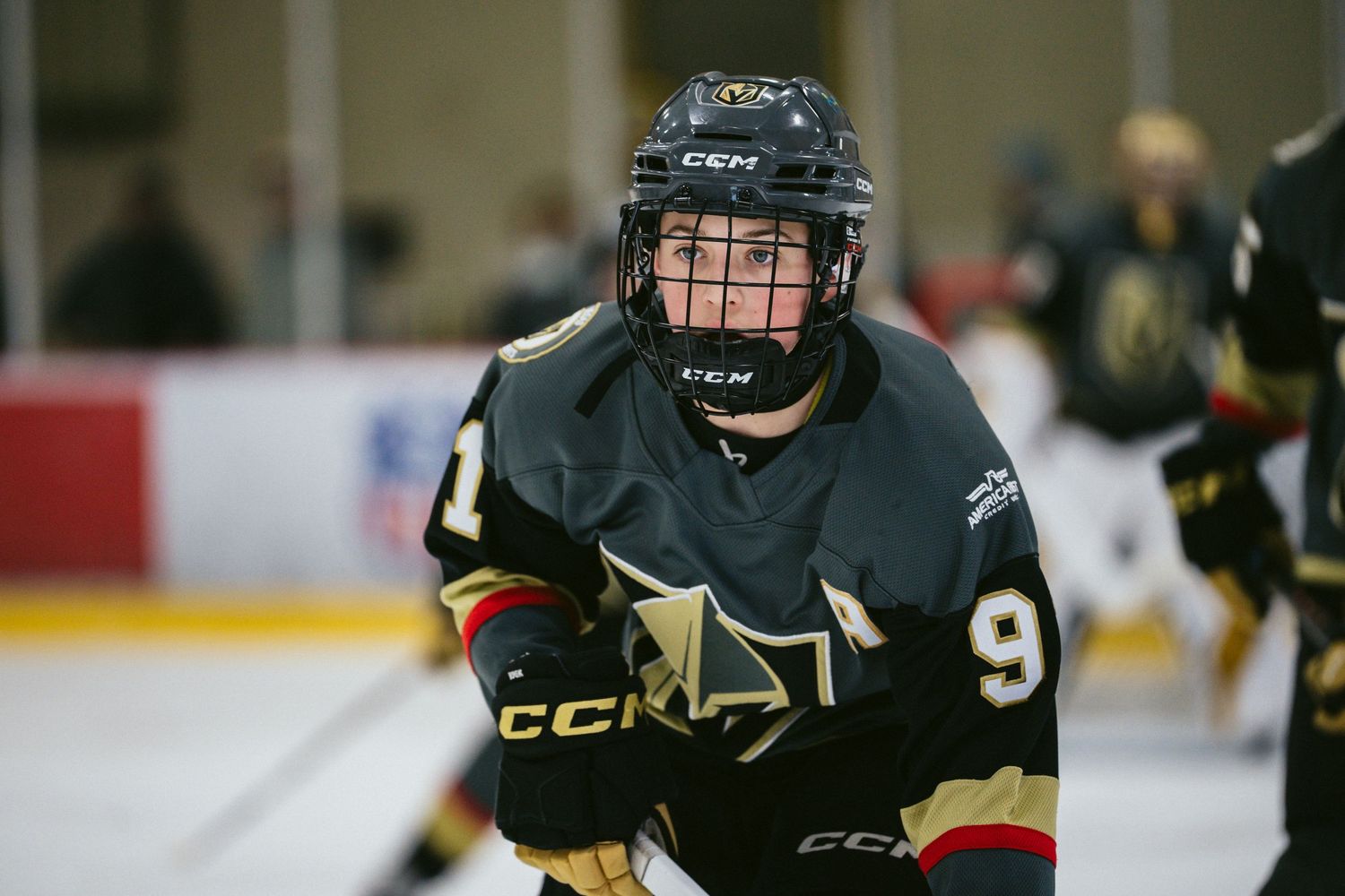 Hockey player in black and gold uniform skates with focus during competitive match.