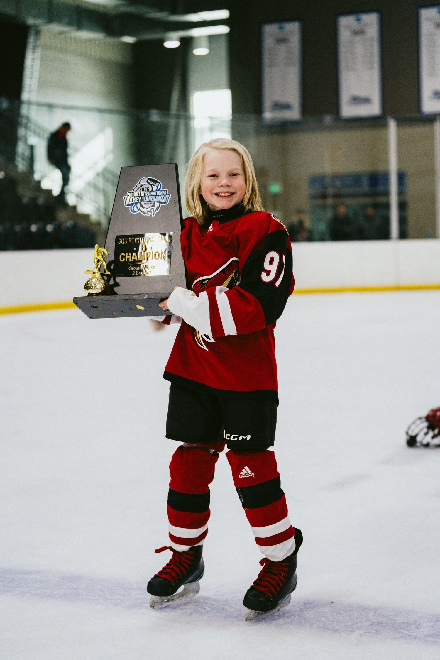 Young hockey player in red uniform proudly displaying championship award on ice.