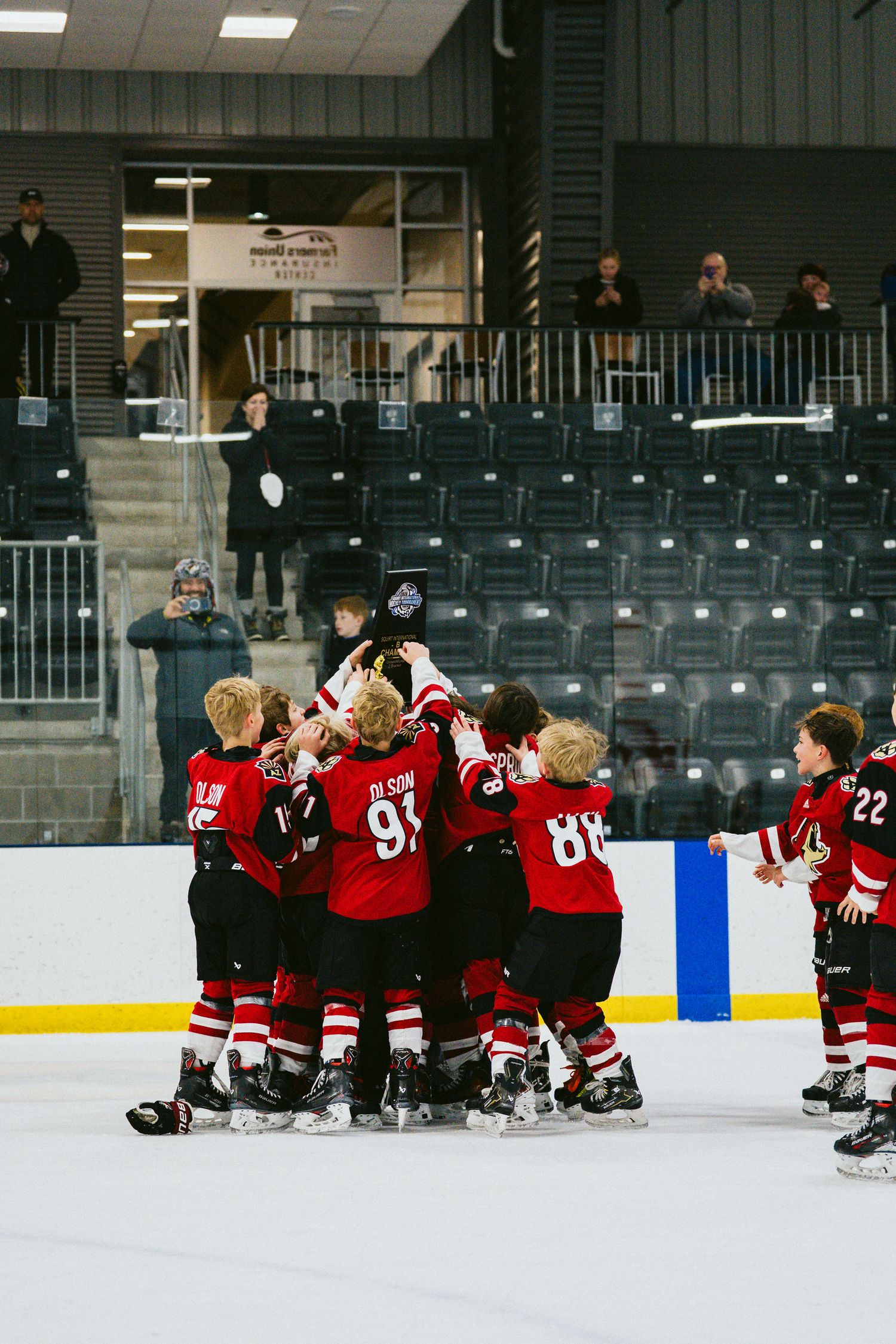 Youth hockey team sitting together on the ice during practice session at indoor arena.