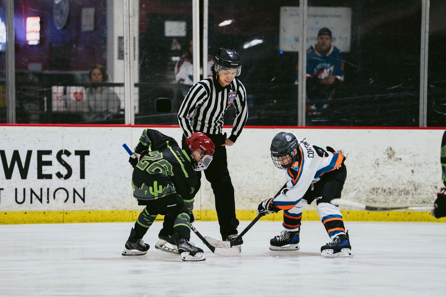 Referee oversees a face-off between two young hockey players during a youth ice hockey game.