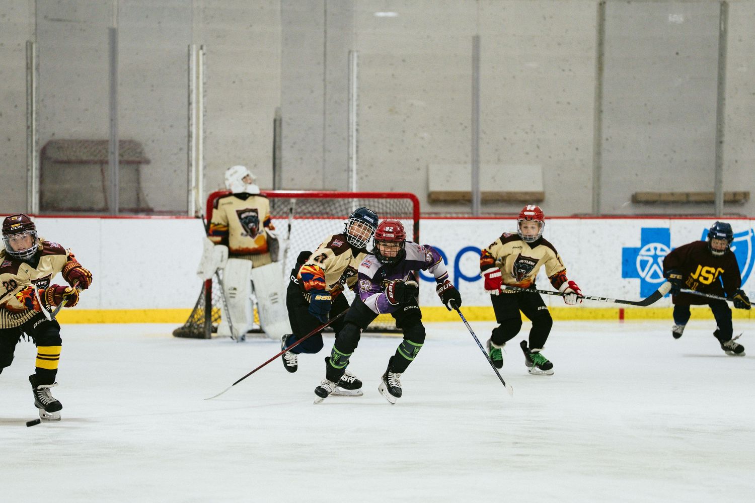 Young hockey players in gold and black uniforms chase the puck during an indoor youth hockey game.