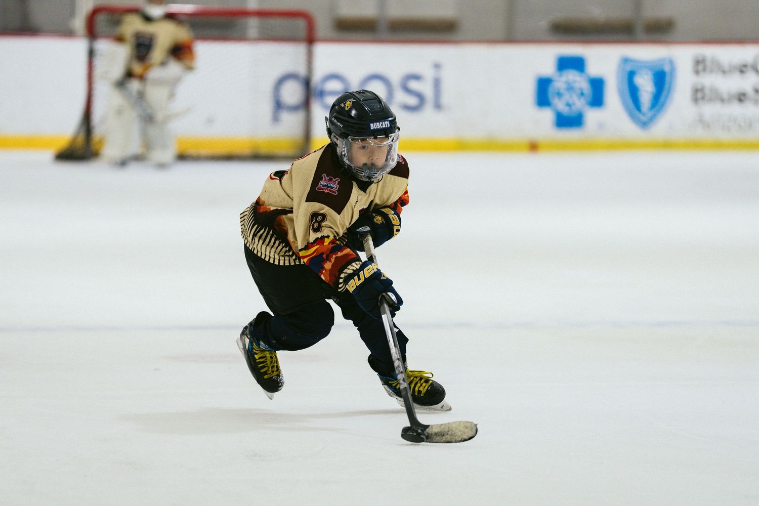 Young hockey player in gold uniform skates with the puck during an indoor ice hockey game.