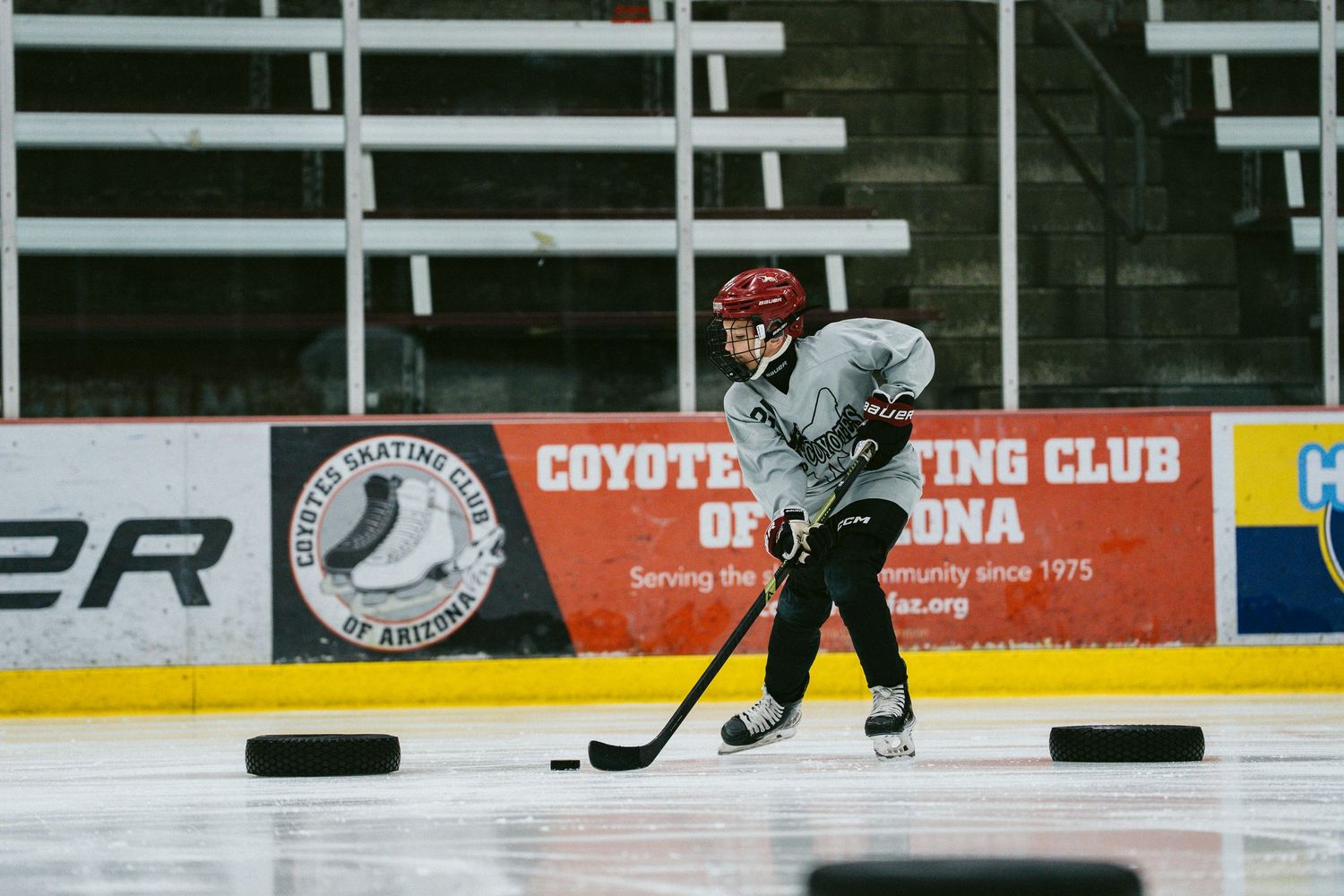 Hockey player skating with a stick and puck on an indoor ice rink at Coyotes Skating Club of Arizona.