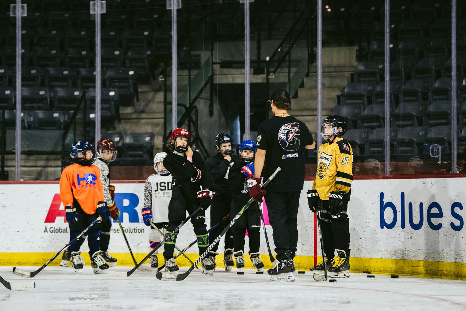 Youth hockey players gather around coach for instruction during ice hockey practice at indoor arena.