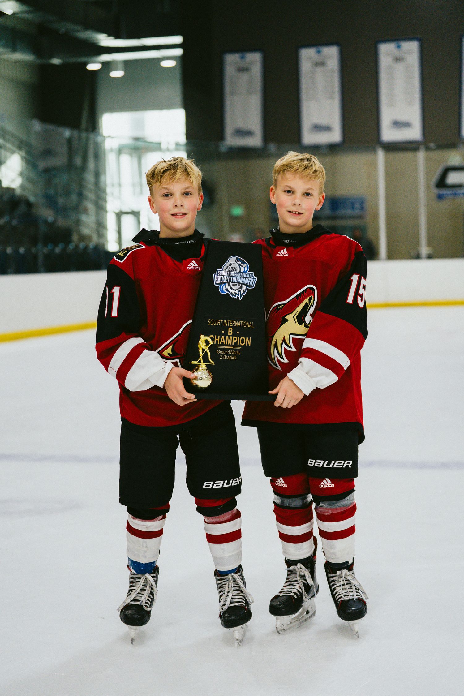 Youth hockey players in red and black uniforms standing together on ice.