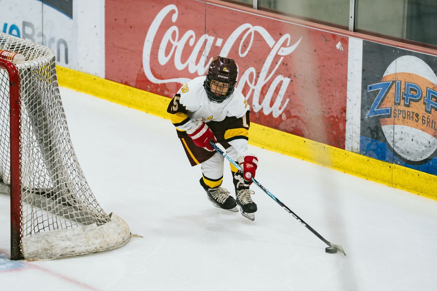Young hockey player skating near the goal during a youth ice hockey game at an indoor rink with Coca-Cola ads.