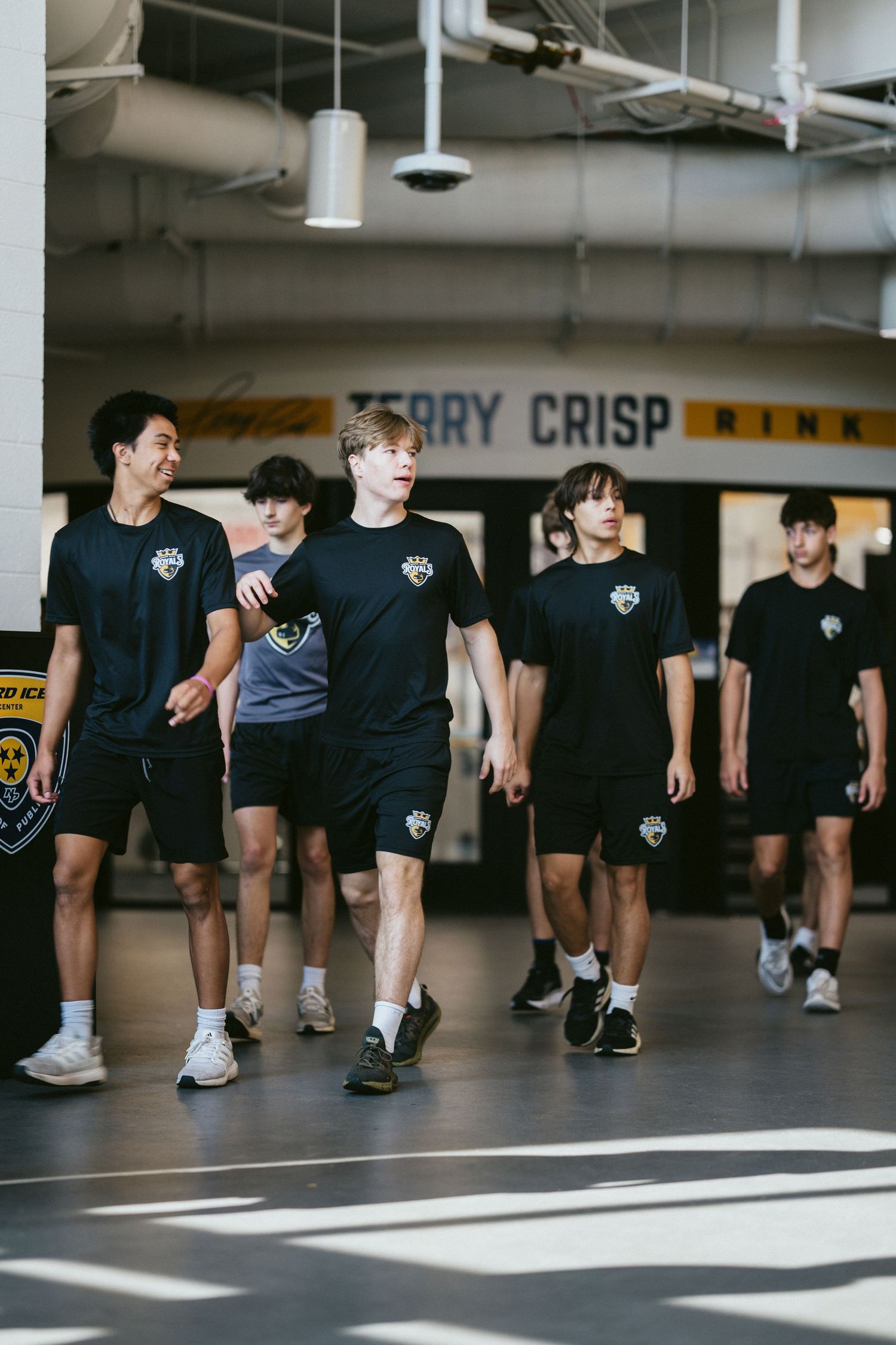 Young hockey players in black team shirts walk through the Terry Crisp Rink facility.
