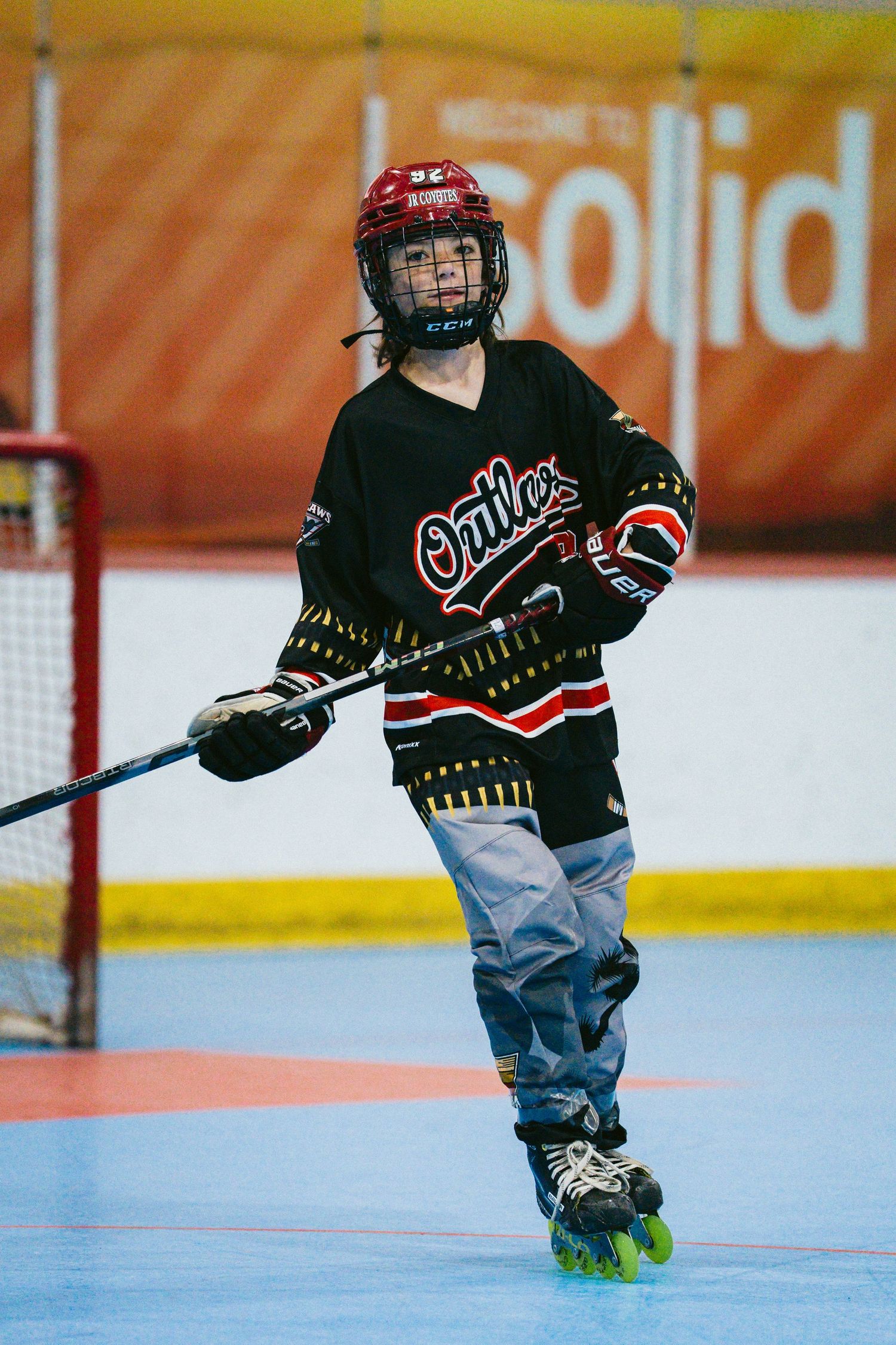 Young roller hockey player in black Oilers jersey and red helmet skating on an indoor rink during a game.