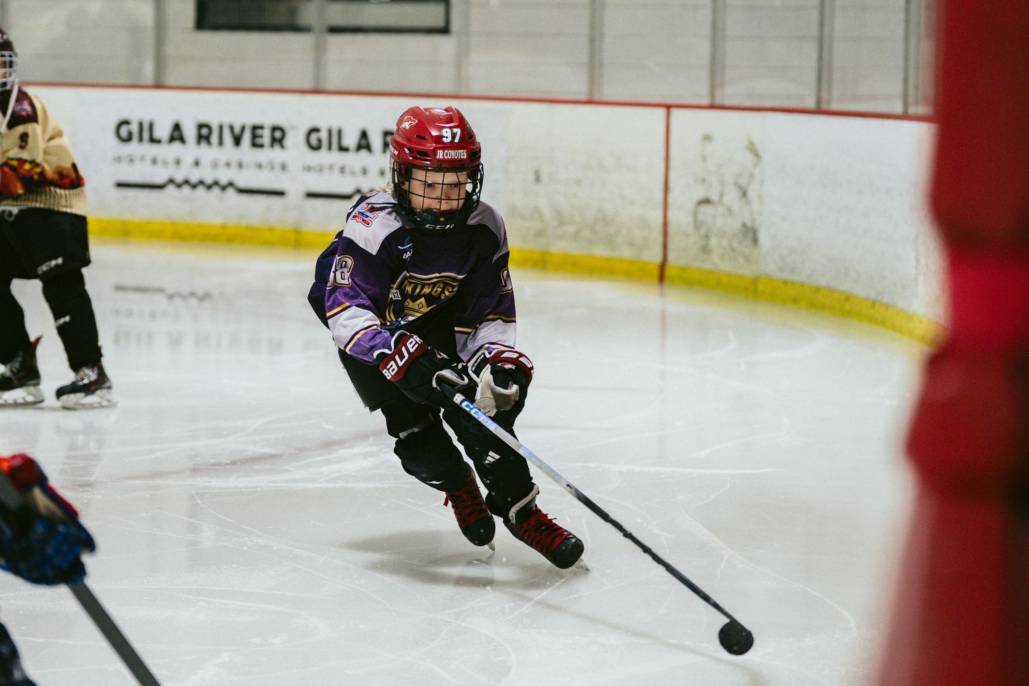 Young hockey player in purple jersey skating with puck on ice rink during youth hockey game.