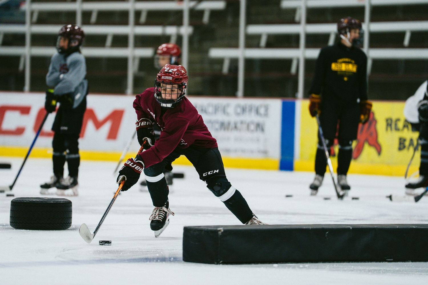Young ice hockey players practice puck handling drills on indoor rink during team training session.