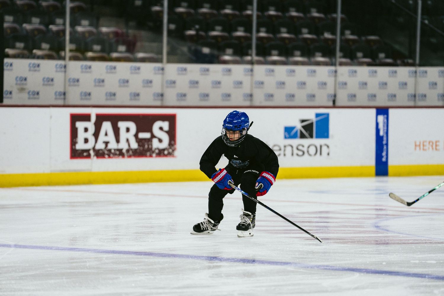Hockey player skating low in a crouch position during practice at an indoor ice rink arena.