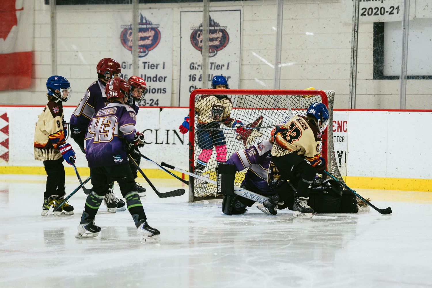 Youth hockey players crowd the net as goalie makes a save during an intense indoor ice hockey game.