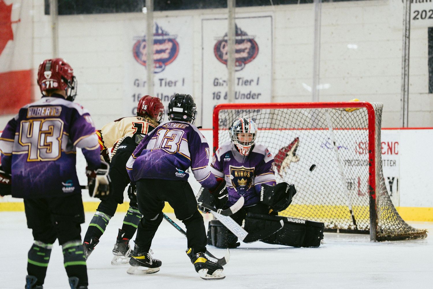 Youth hockey players crowd the net during an exciting goal attempt in an indoor rink.