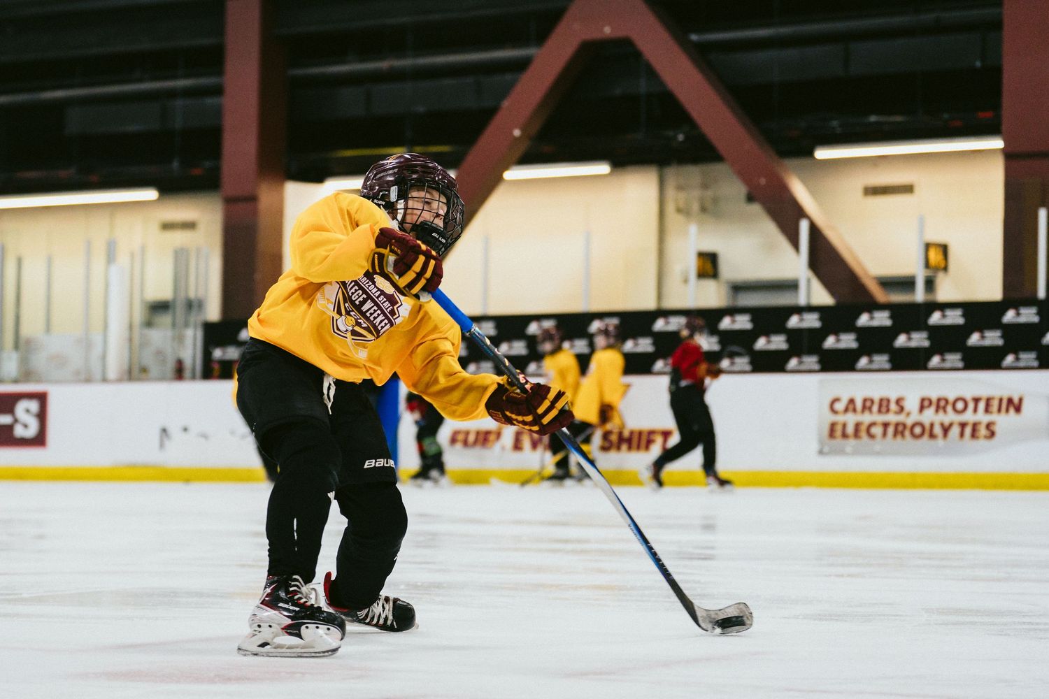 Youth hockey player in yellow jersey handles puck during indoor ice hockey practice session.
