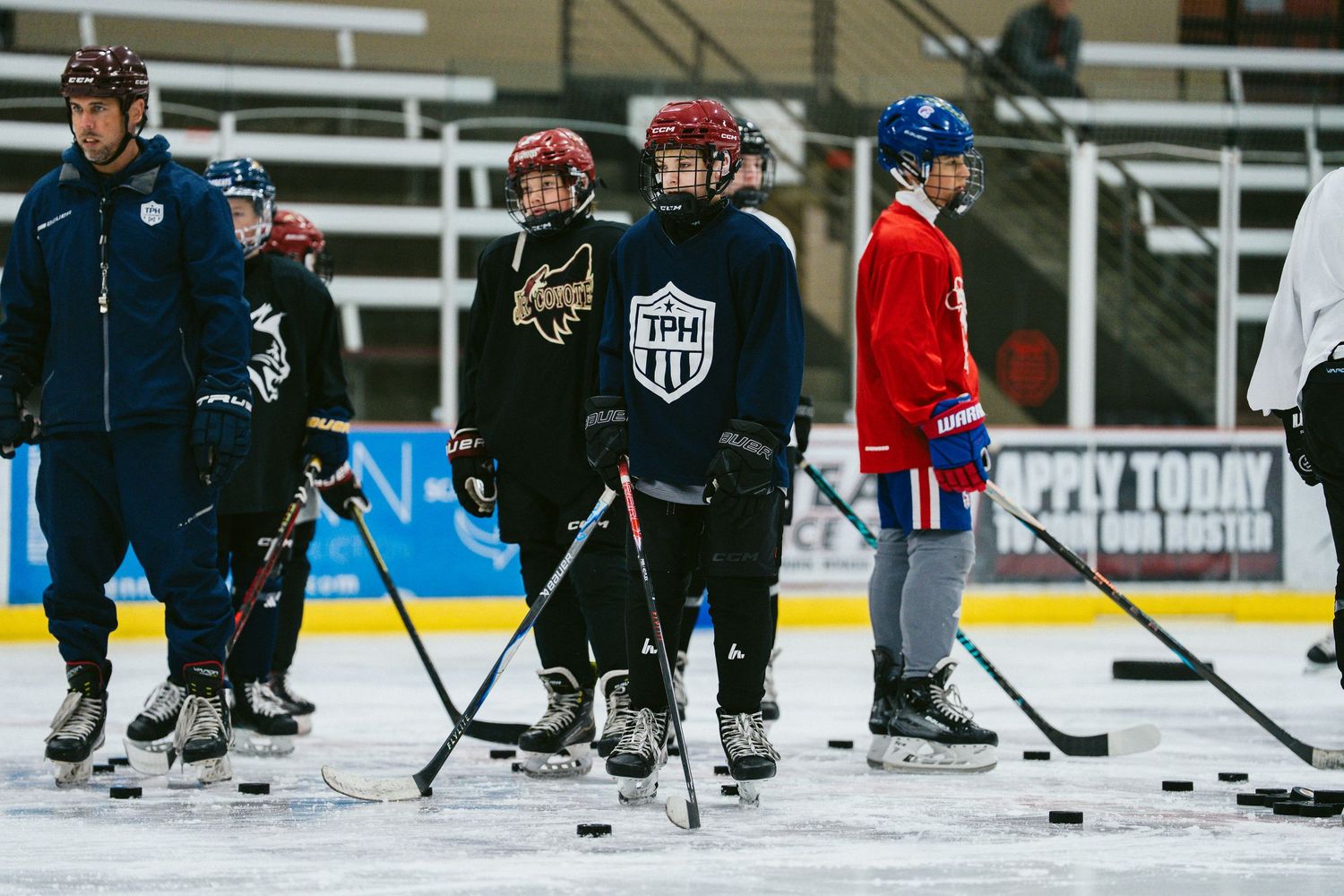 Young hockey players in full gear stand on the ice during a youth hockey practice at an indoor arena.