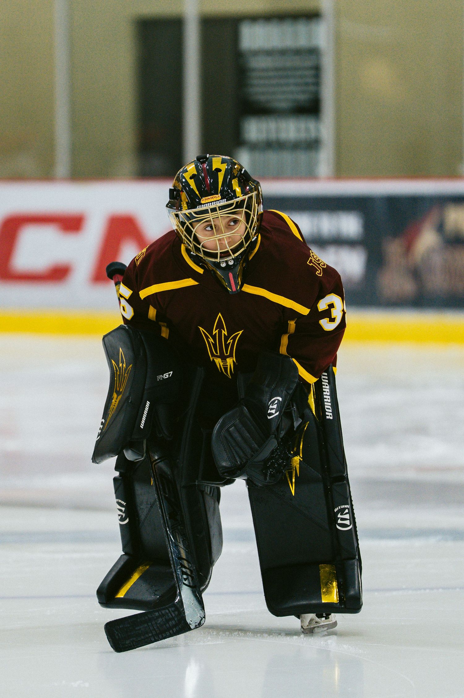 Hockey goalie in black and gold uniform crouches low on the ice during game action.