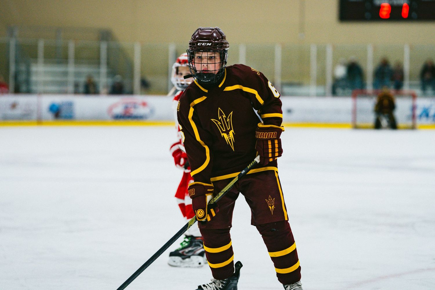 Youth hockey players in brown and red uniforms skating during competitive game.
