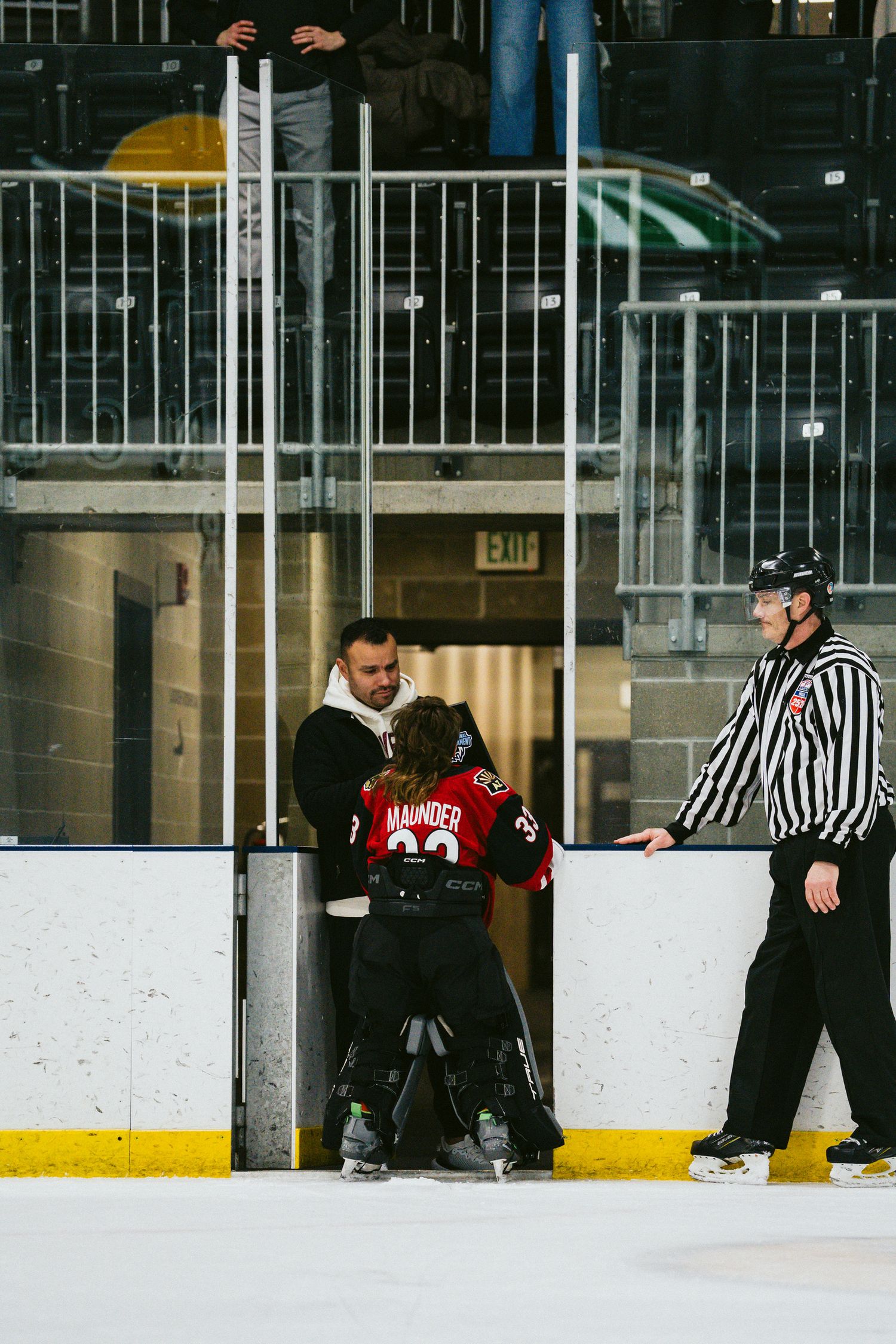 Officials in referee uniforms observing activity on indoor hockey rink.