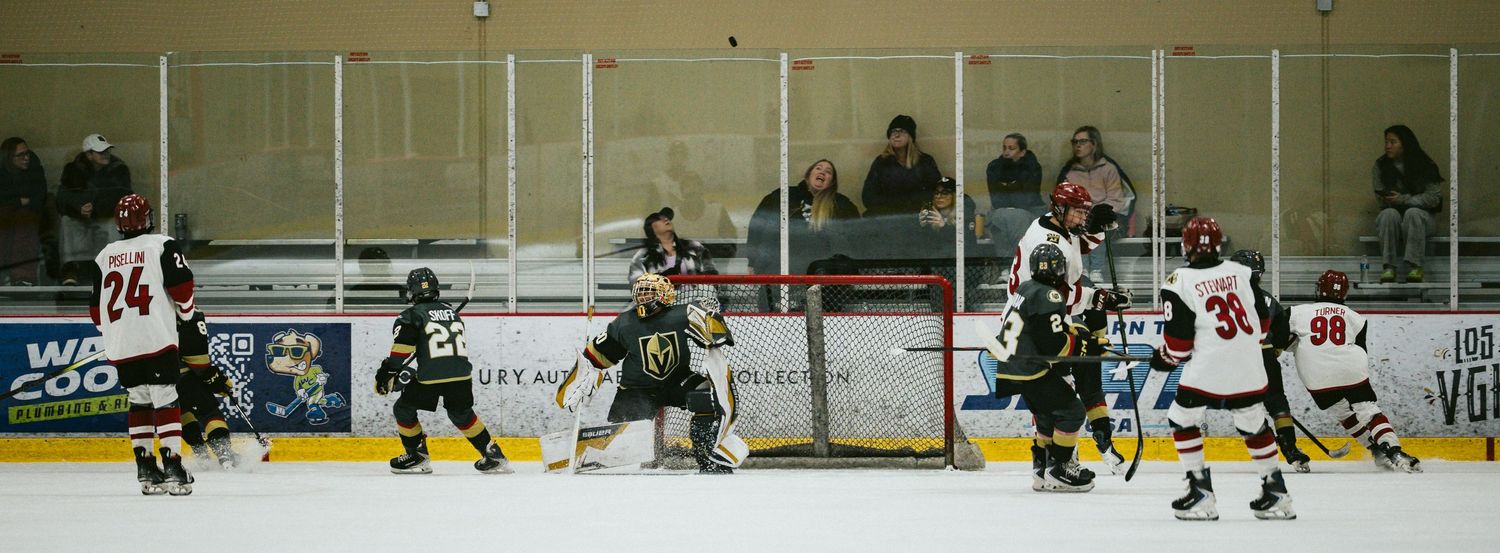 Wide angle view of hockey players competing on ice with arena boards visible in the background.