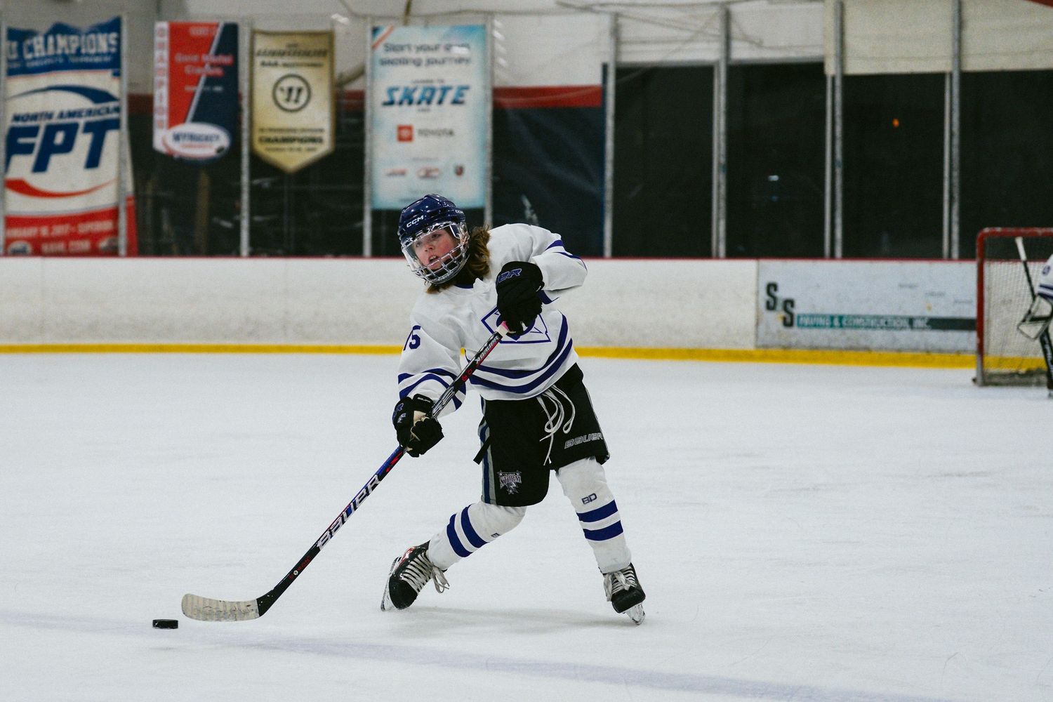 Hockey player in white and blue uniform skates with puck on ice rink.