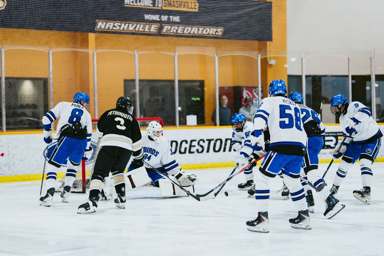 Blue and white hockey team attacks the goal during an intense indoor ice hockey game.