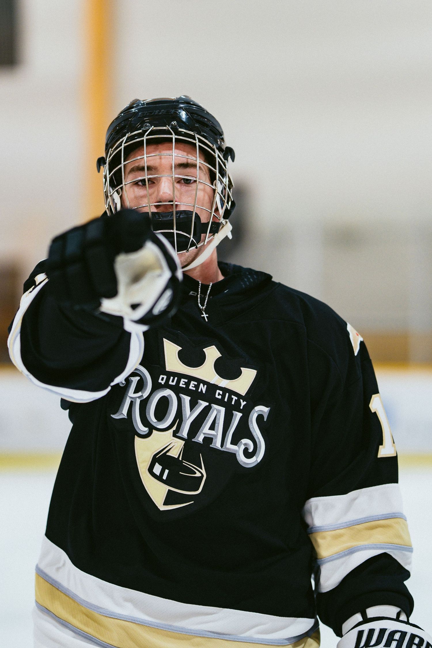 Young hockey player in Queen City Royals black jersey and helmet pointing on ice rink during game.