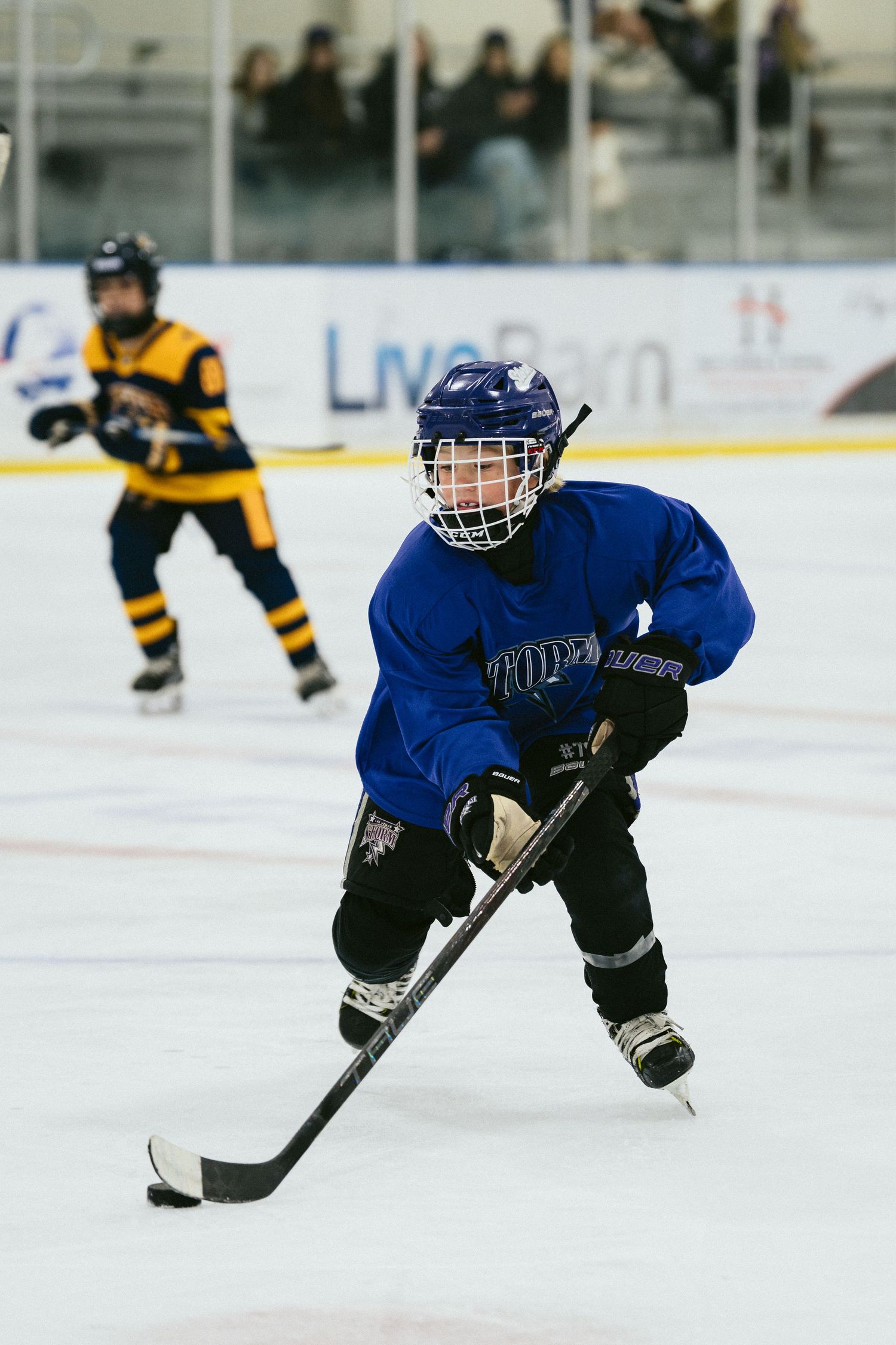 Young ice hockey player in blue jersey controls puck during youth hockey game on indoor rink.