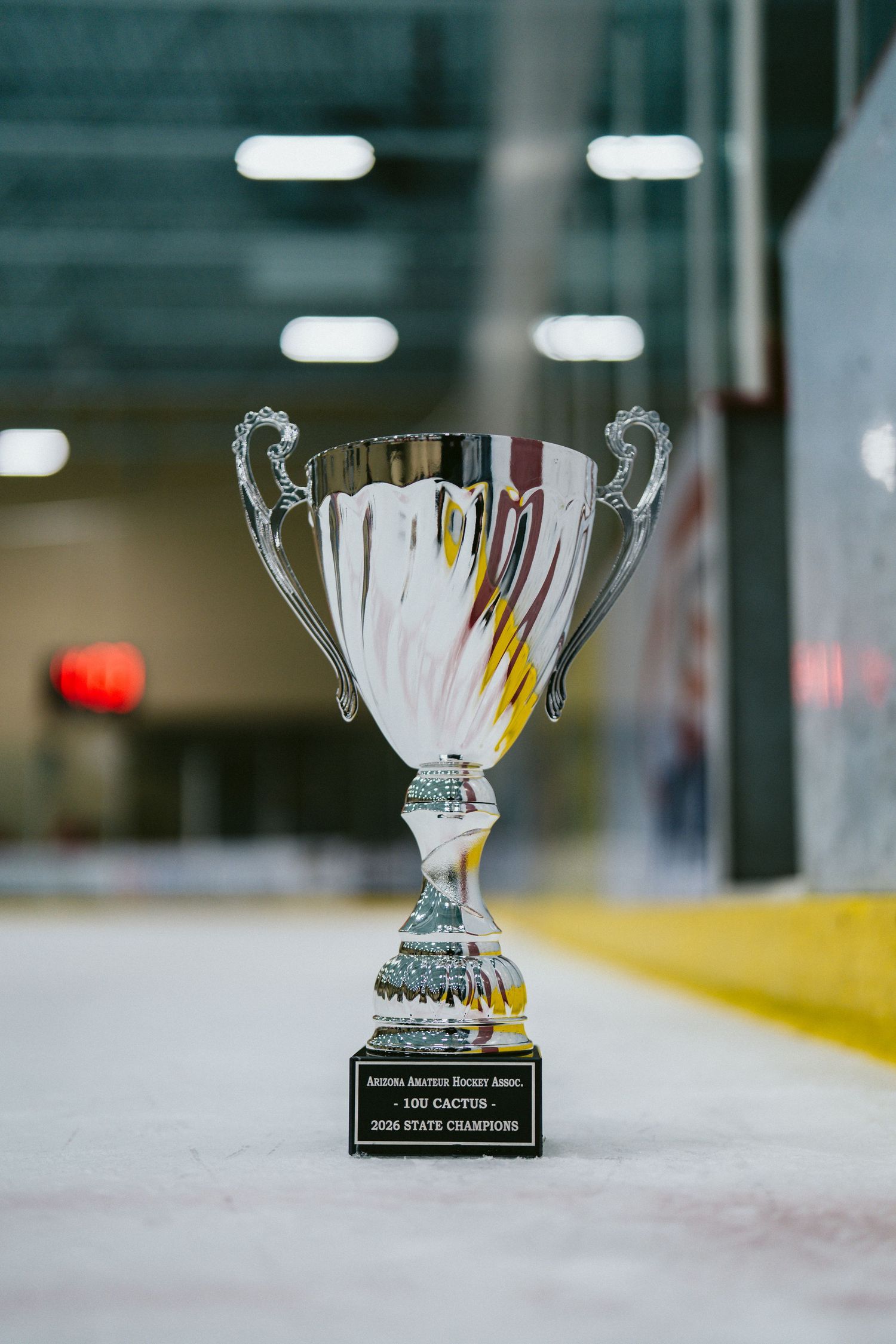 Silver championship trophies displayed on the boards of an ice hockey rink.