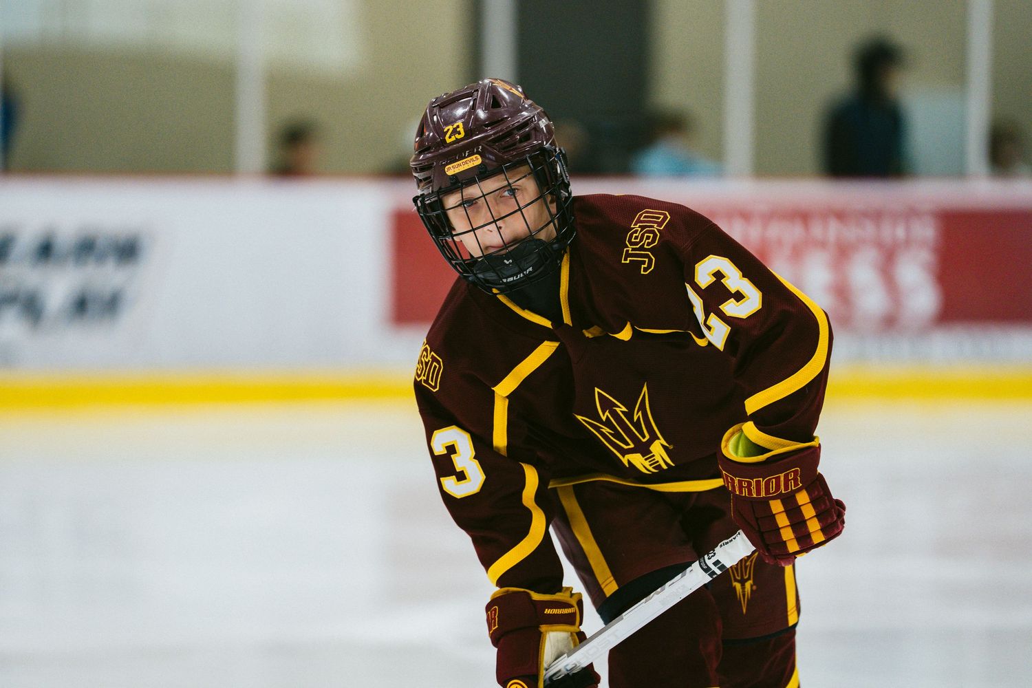 Hockey player in brown and gold uniform skates with stick during competitive match on ice rink.