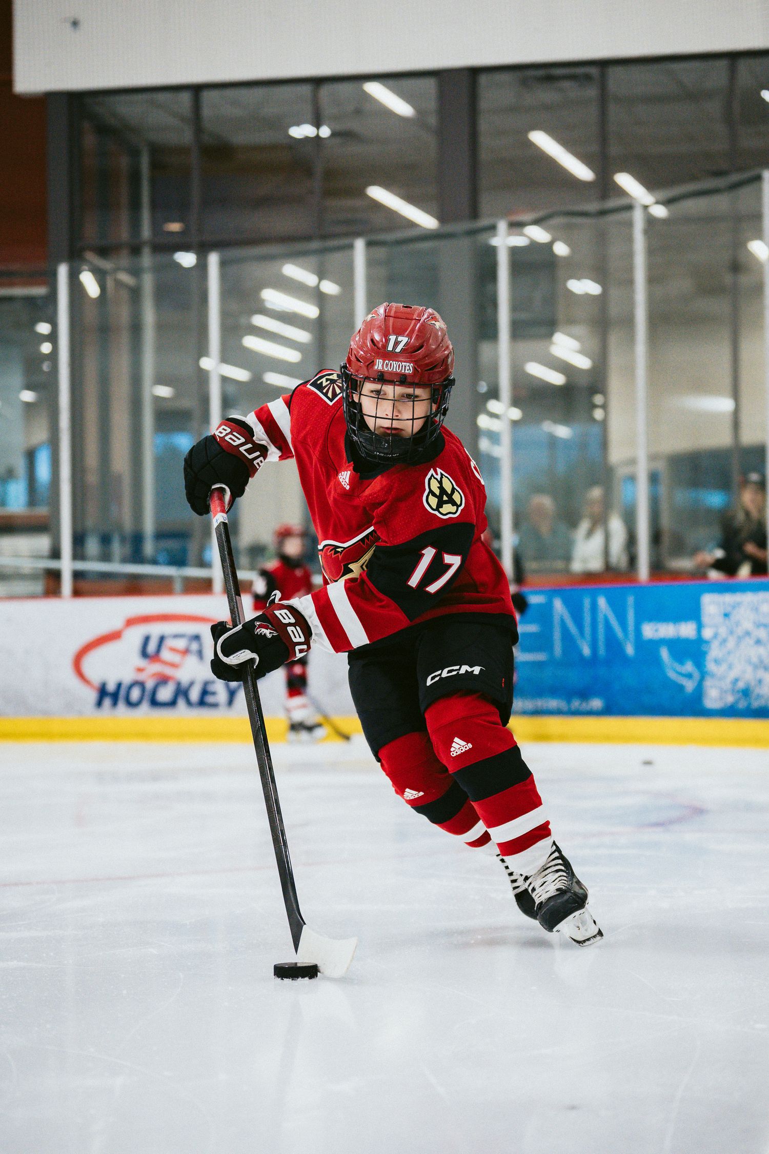 Hockey player in red uniform performs acrobatic diving move on ice rink.