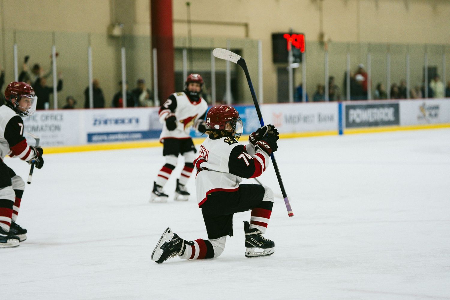 Hockey players in action on ice rink with spectators watching from behind glass.
