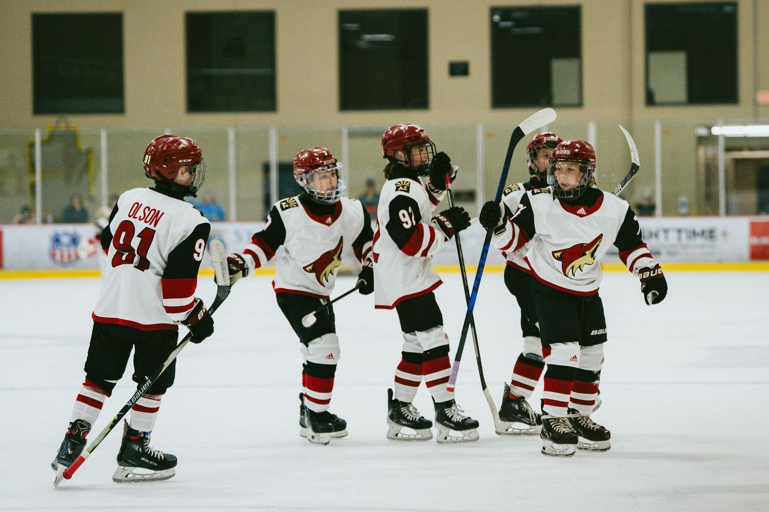 Youth hockey players line up on the ice during a game, wearing red and green jerseys with white accents.