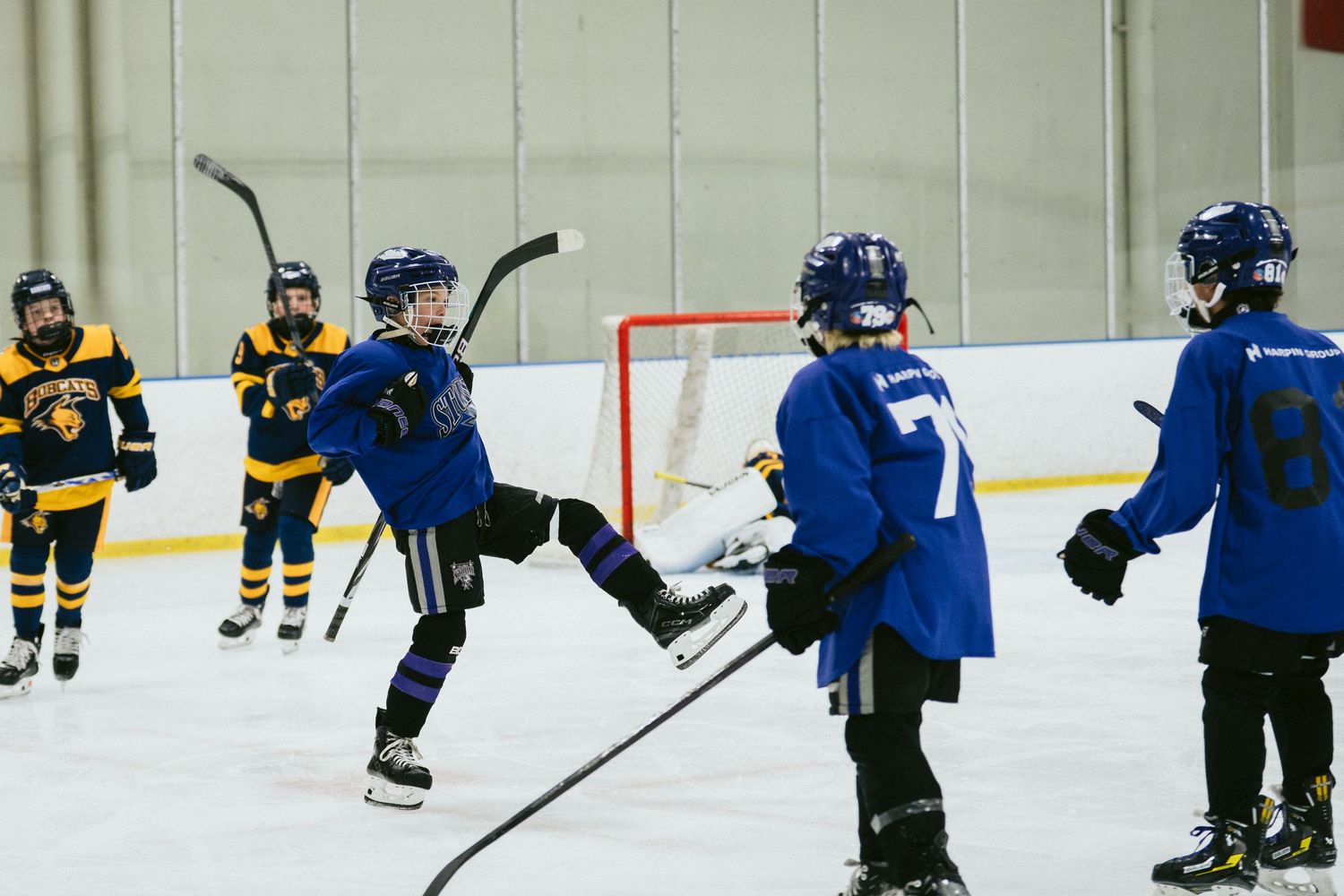 Young hockey players in blue and yellow uniforms compete on an indoor ice rink during a youth hockey game.