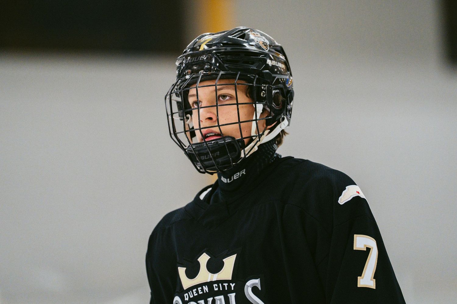 Young hockey player wearing a Queen City Royals jersey and protective helmet during a game.