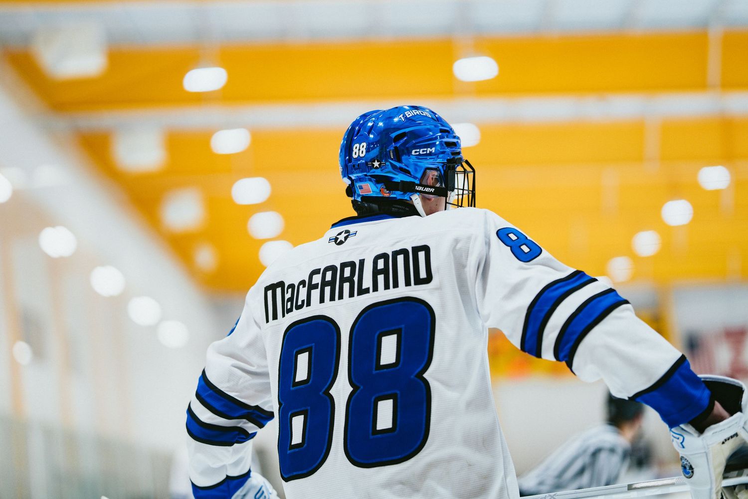 Hockey player MacFarland wearing number 88 in blue and white jersey stands at the rink boards.