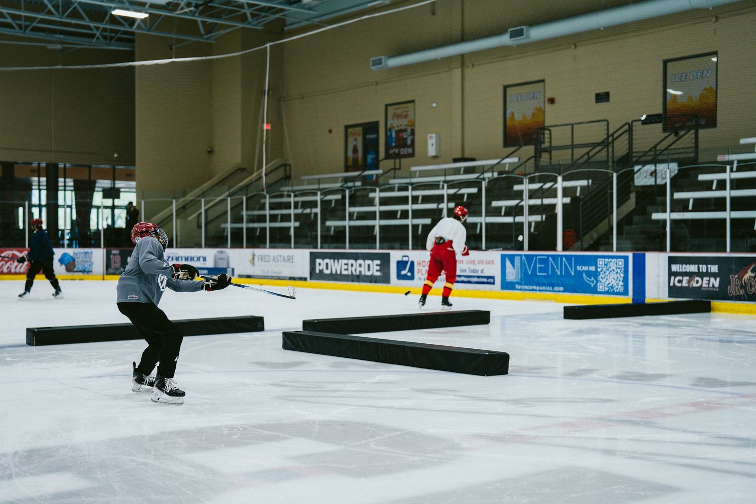Two hockey players practice skating drills on an indoor ice rink with black obstacles on the ice.