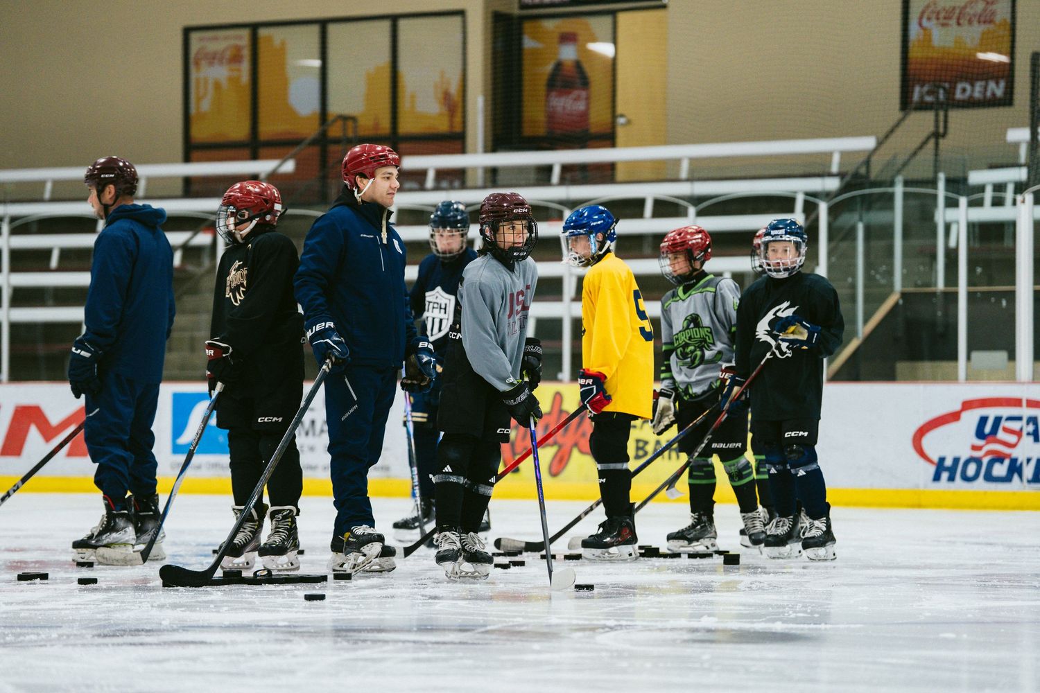 Youth hockey players practice on indoor ice rink with coaches during USA Hockey training session.