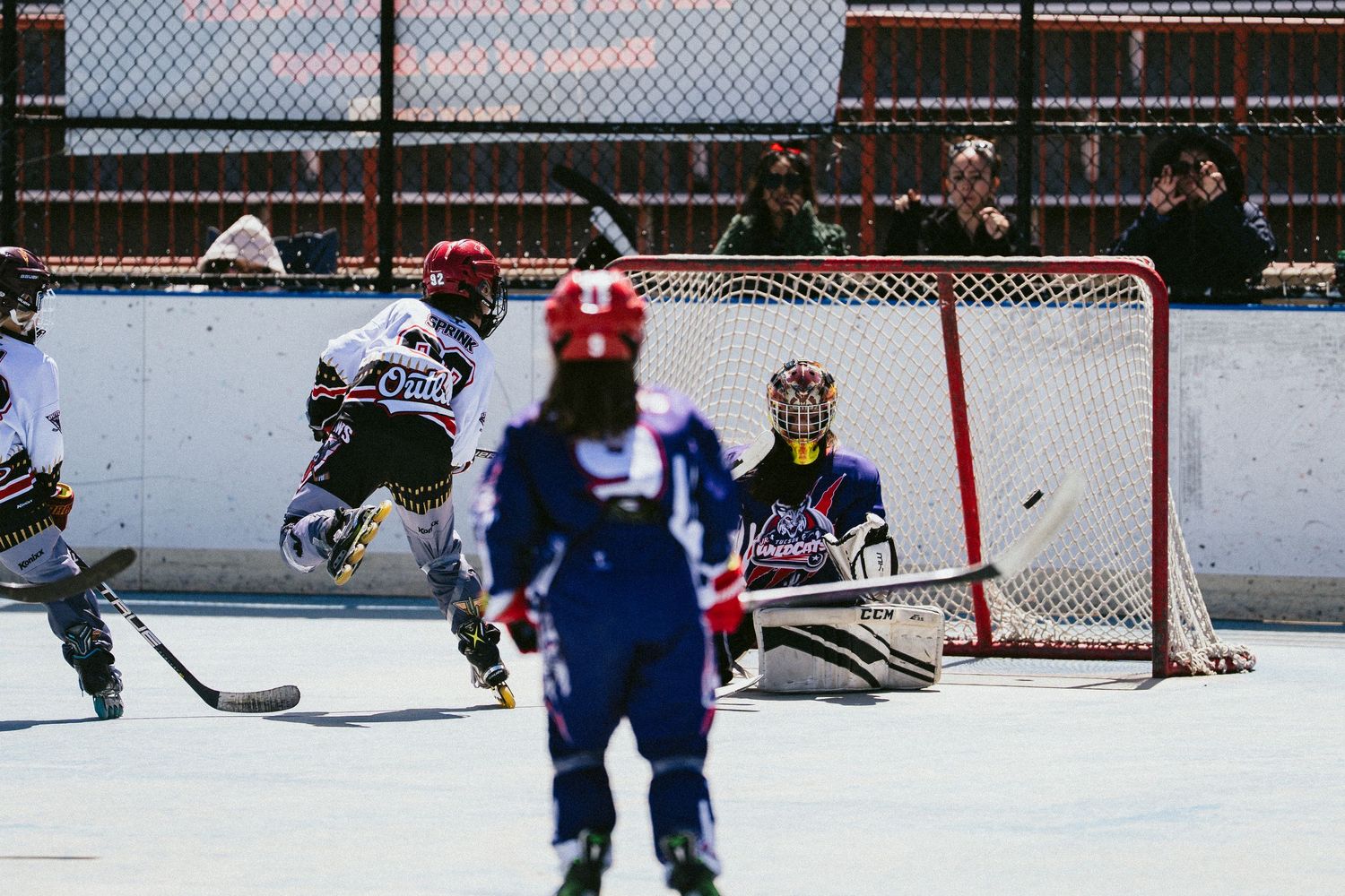 Youth hockey players compete in an outdoor rink game, with a goalie defending the net during an exciting match.