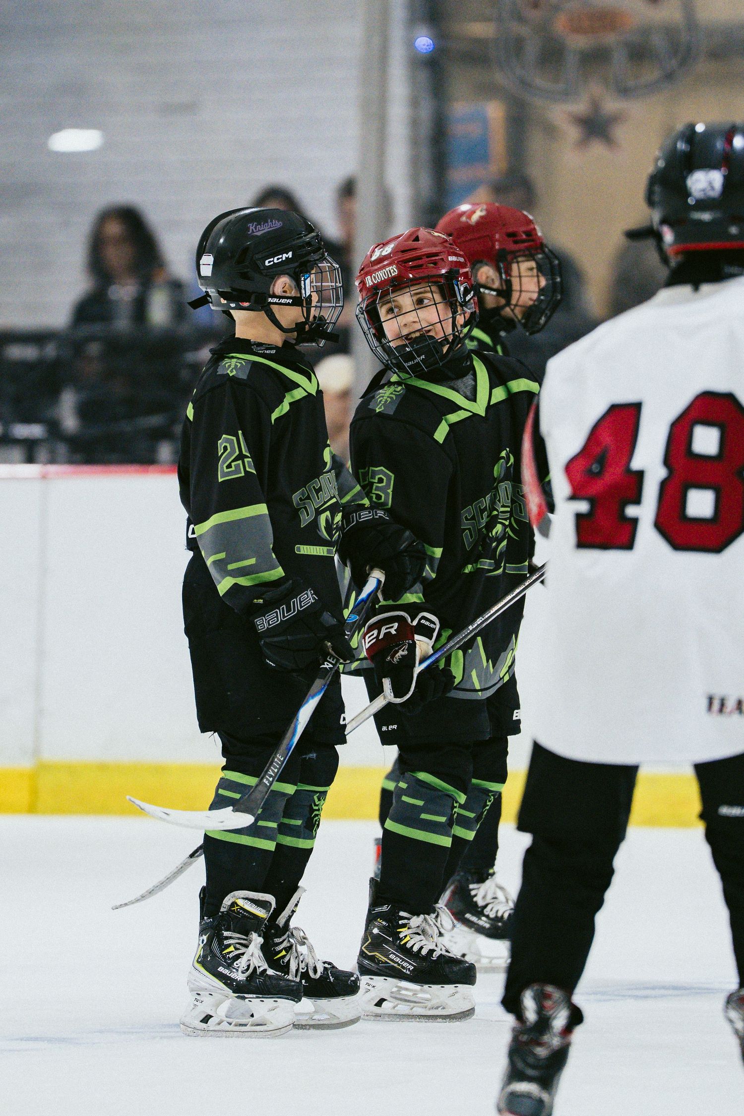 Young hockey players in black green uniforms interact with opponent wearing number 48 jersey.