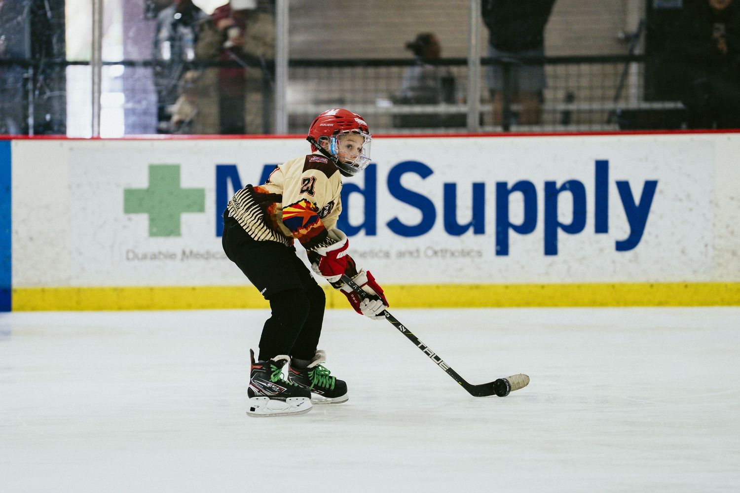 Young hockey player in black and gold jersey skating with stick during youth ice hockey game.