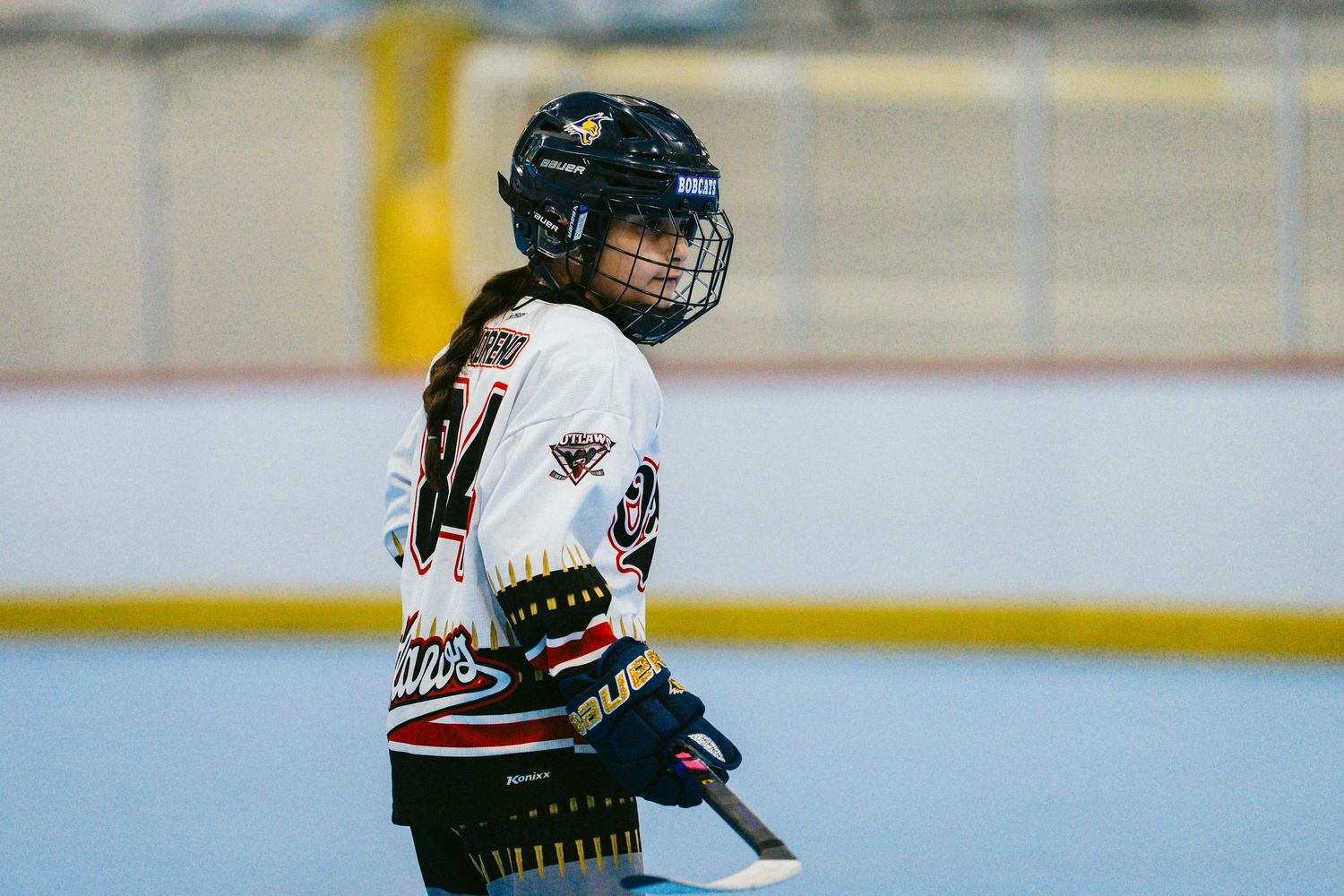 Young roller hockey player in white Outlaws uniform holds a stick during an indoor inline hockey game.