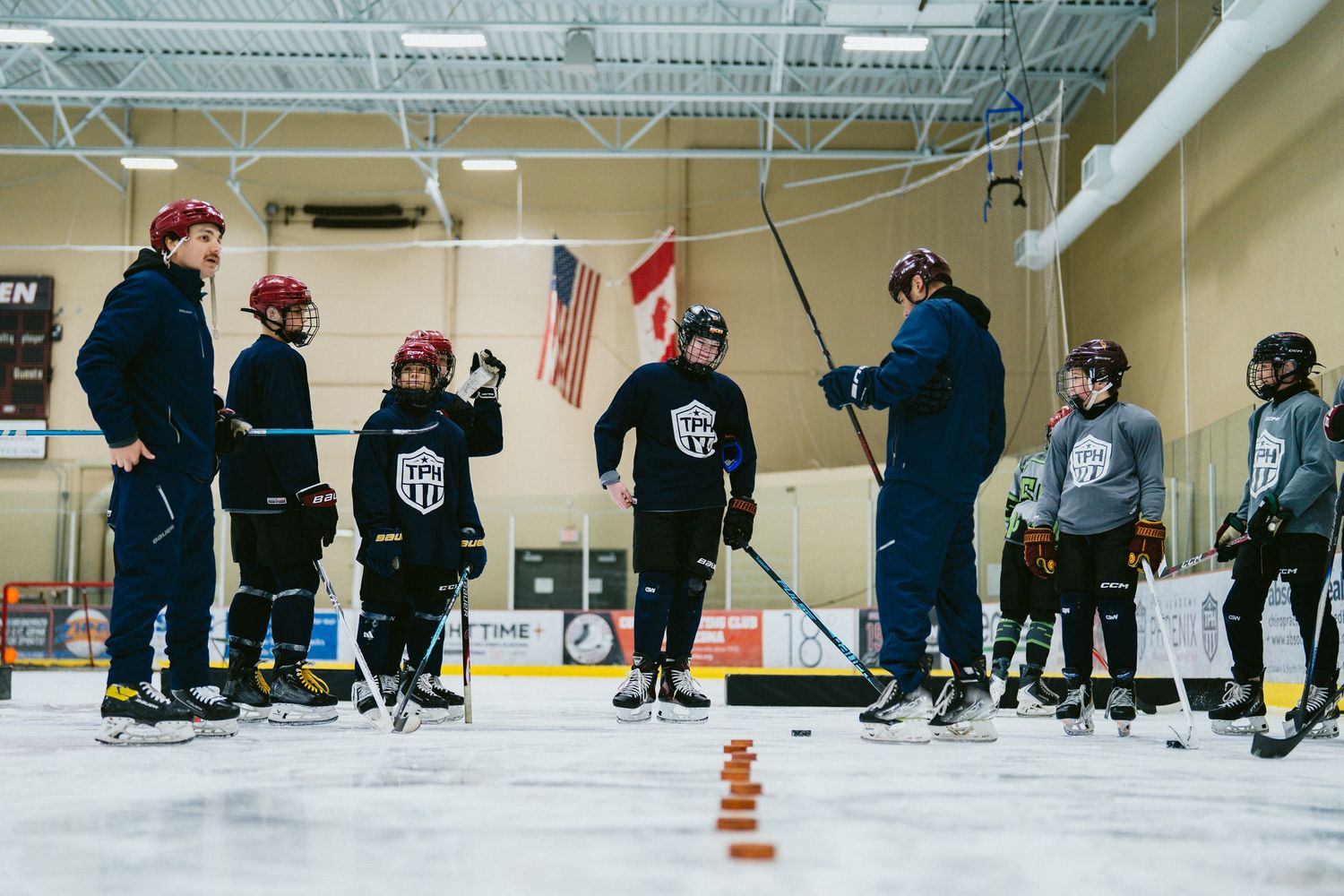 Hockey coach instructing group of young players on ice rink during training drill.