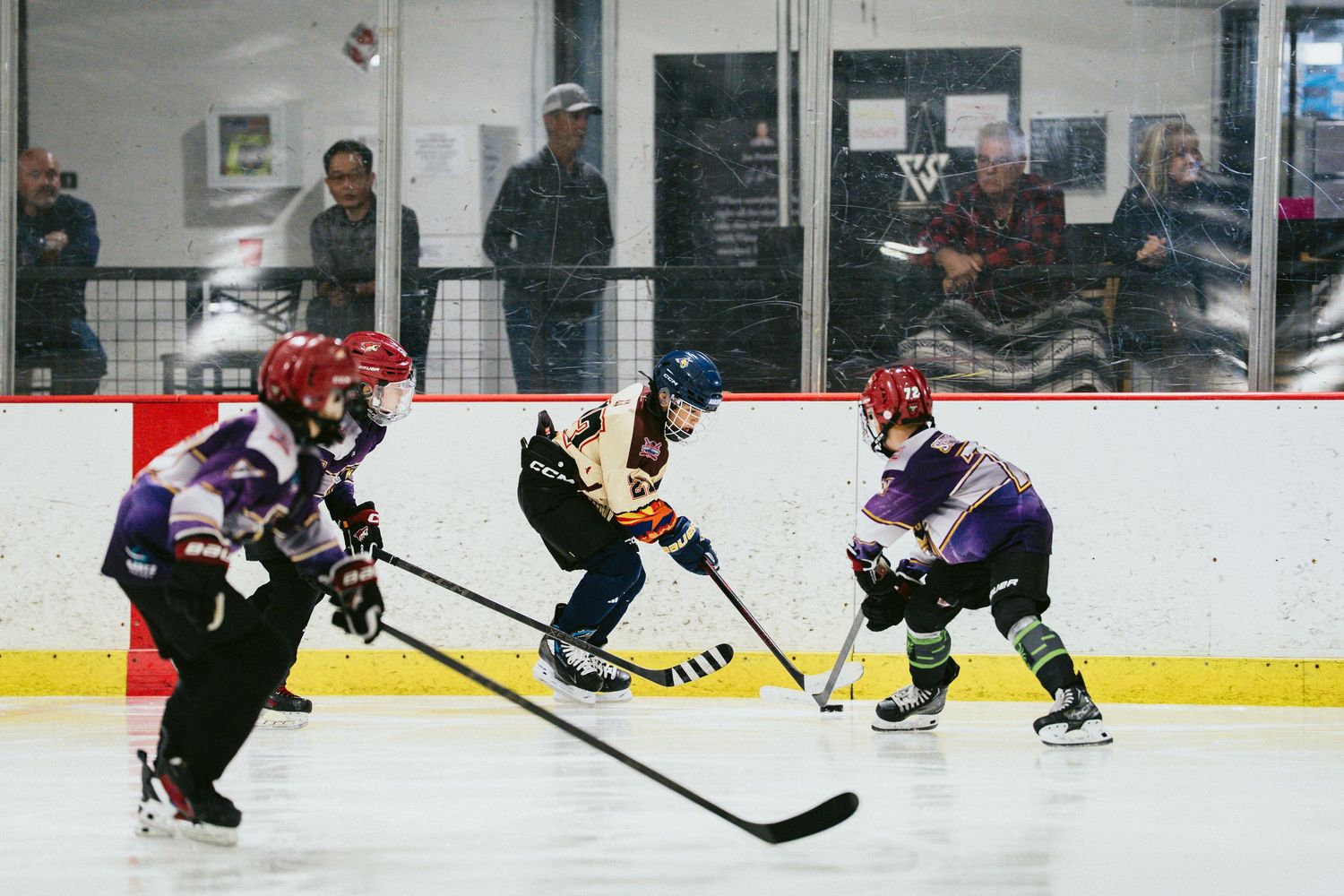 Three young hockey players battle for the puck during an intense youth ice hockey game.
