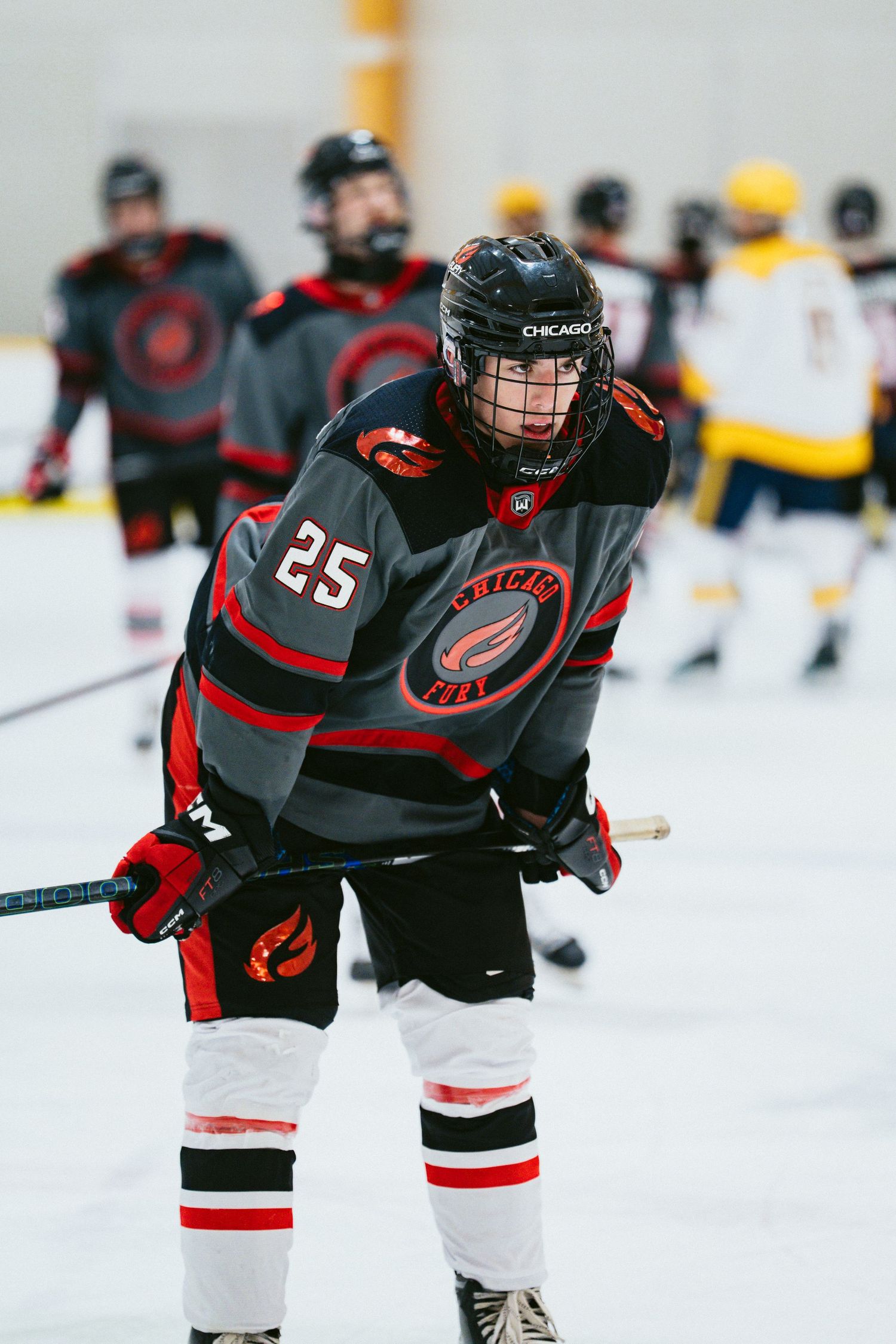 Hockey player number 25 in a Chicago Fire black jersey skates on indoor ice rink during a competitive game.