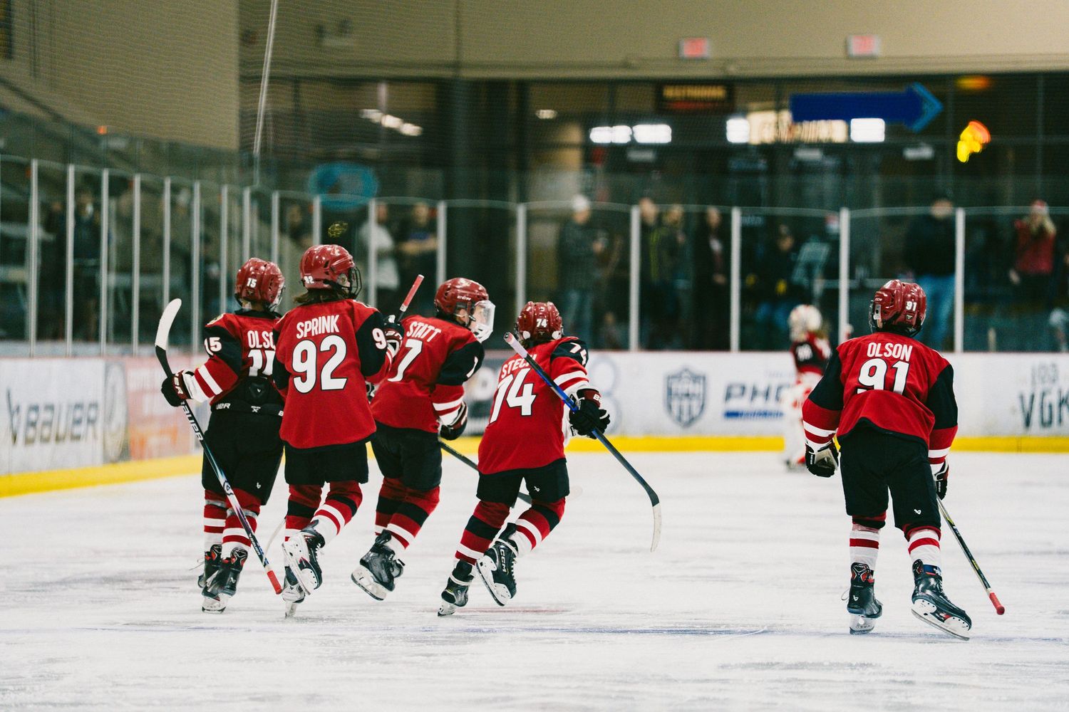 Hockey players in red jerseys practicing drills and skating on an indoor ice rink during training.